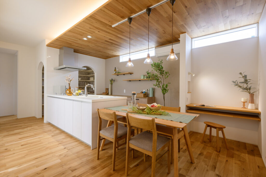 木目の天井とペンダントライトが印象的な、白いキッチンとダイニングテーブルのあるナチュラルなLDK