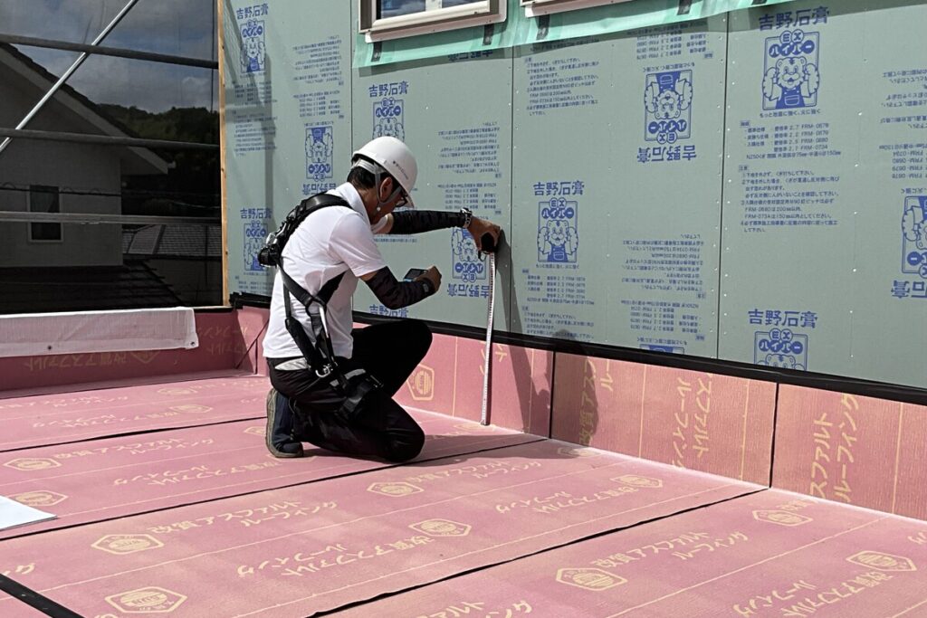 住宅の建築現場で、メジャーを使って防水シートや壁材の施工精度を厳密にチェックする技術者。