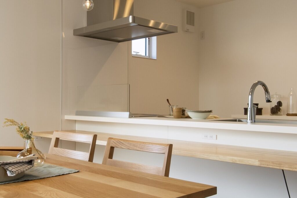 白を基調とした清潔感のある対面キッチンと、温かみのある木のダイニングテーブル。契約前に生活動線を確認するための内観イメージ。