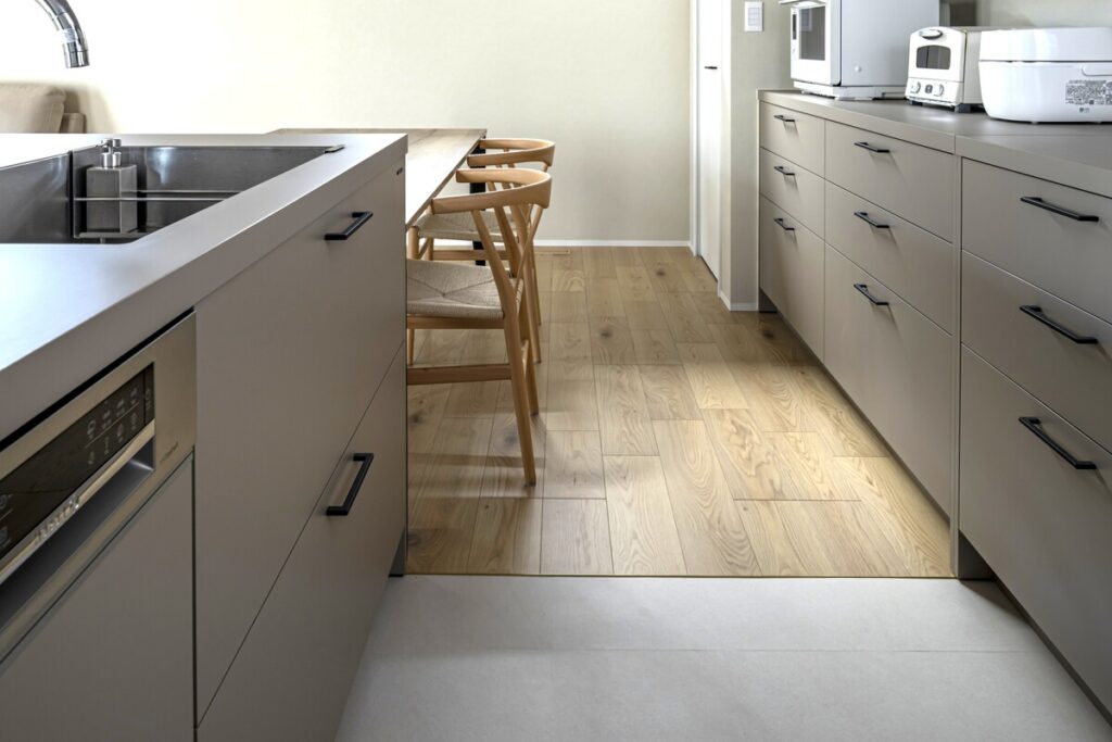 グレージュのシステムキッチンと背面の大型収納、温かみのある無垢フローリング