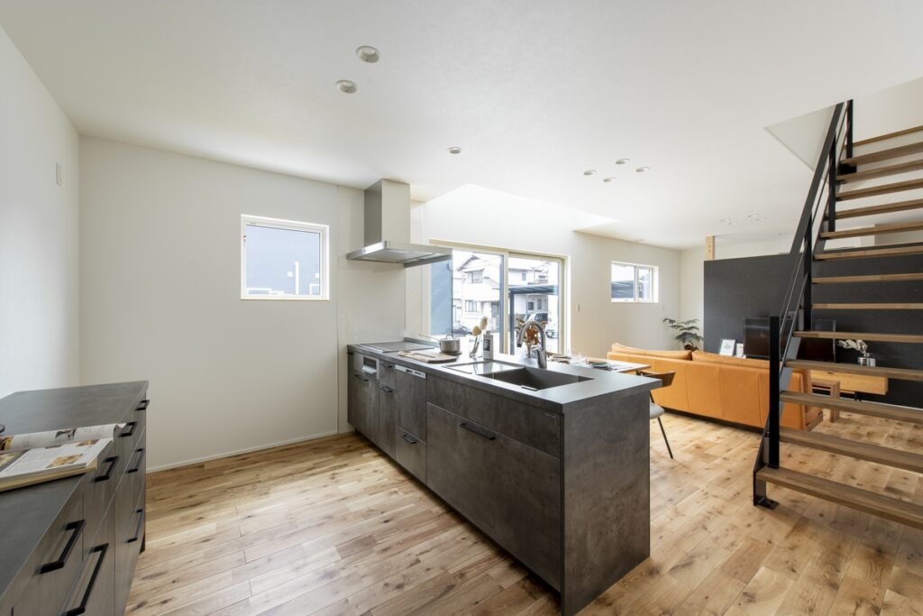 自然光が差し込む明るいLDKに設置された、グレーの石目調キッチンカウンターと無垢材フローリングのインテリア