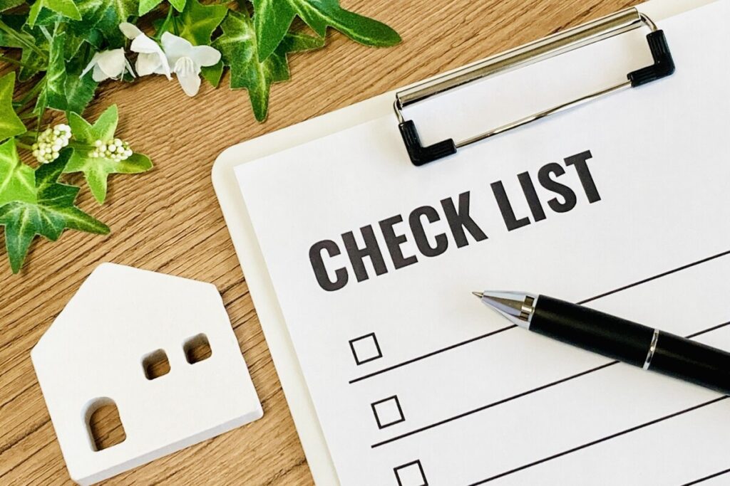 チェックリストとペン、住宅模型が置かれたデスク。耐震等級3の内容を確認するための事前チェックのイメージ