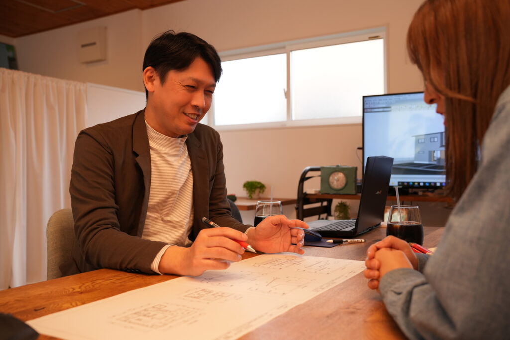 実物の住宅間取り図を広げ、笑顔で打ち合わせをする家咲の建築士とお客様。山口県での理想の注文住宅づくり。