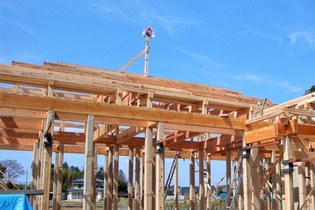 青空の下で進む、木造住宅の基礎と柱が組み上がった家づくりの建築現場。