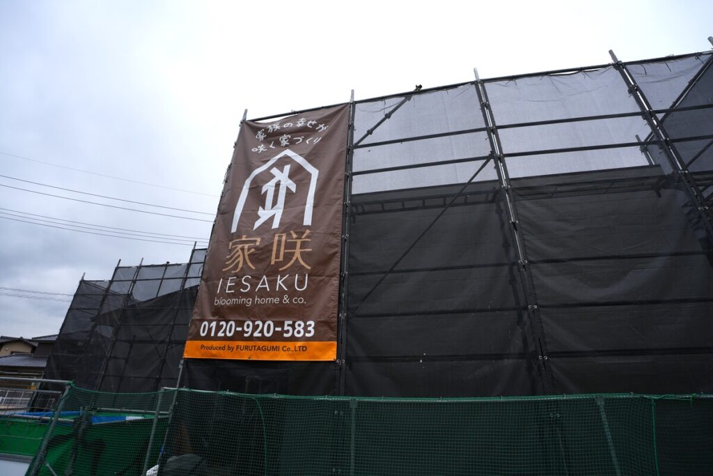 「家咲 IESAKU」のブランドロゴが掲げられた建築現場の足場と飛散防止ネット