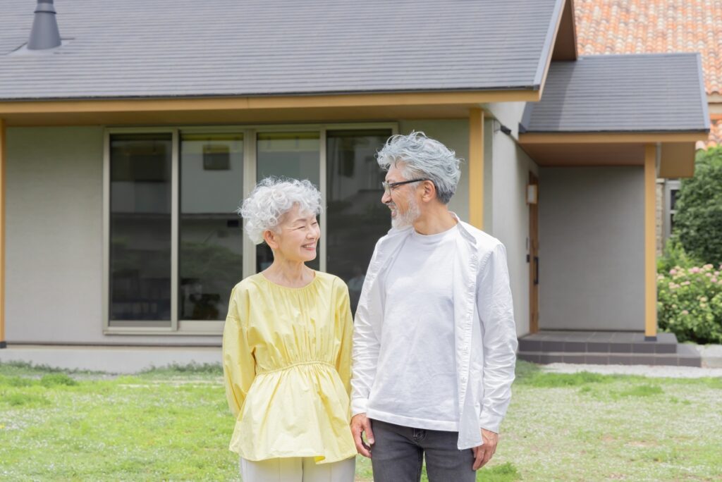 庭の緑が豊かな平屋住宅の前で、仲睦まじく見つめ合うシニア世代の夫婦。