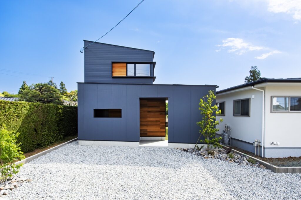 グレーの外壁と木目が調和した住宅の広い砂利敷き駐車場
