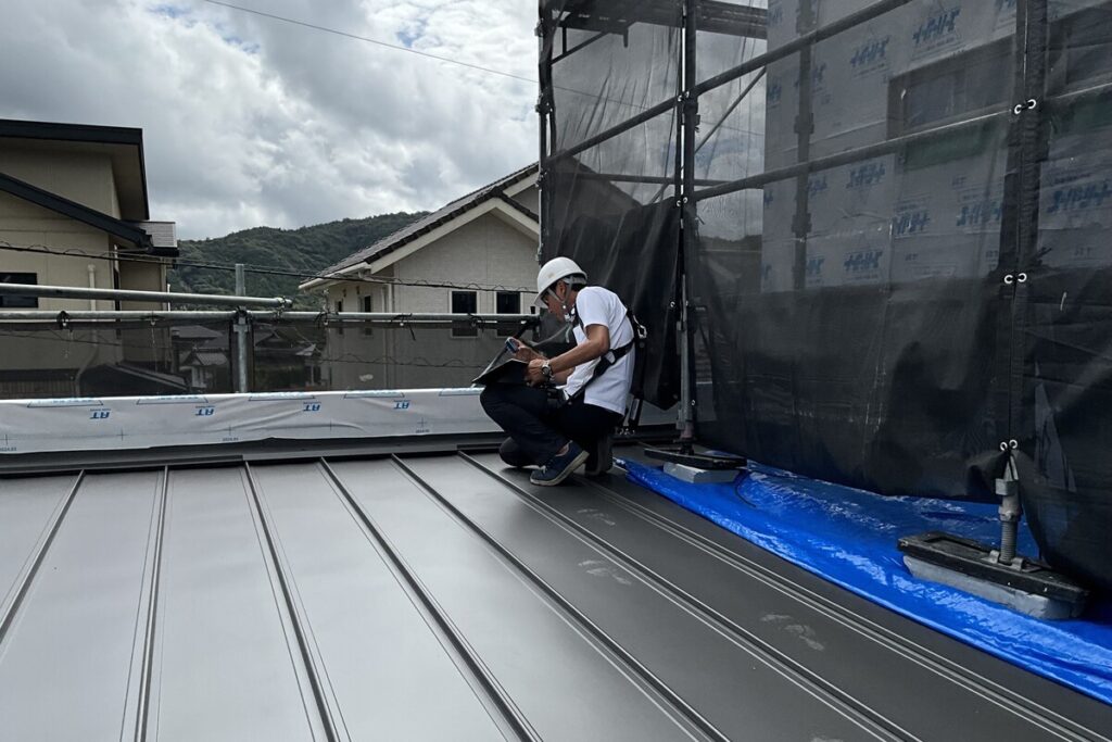 ヘルメットを着用し、屋根の上でガルバリウム鋼板の施工状況を記録・点検する技術者