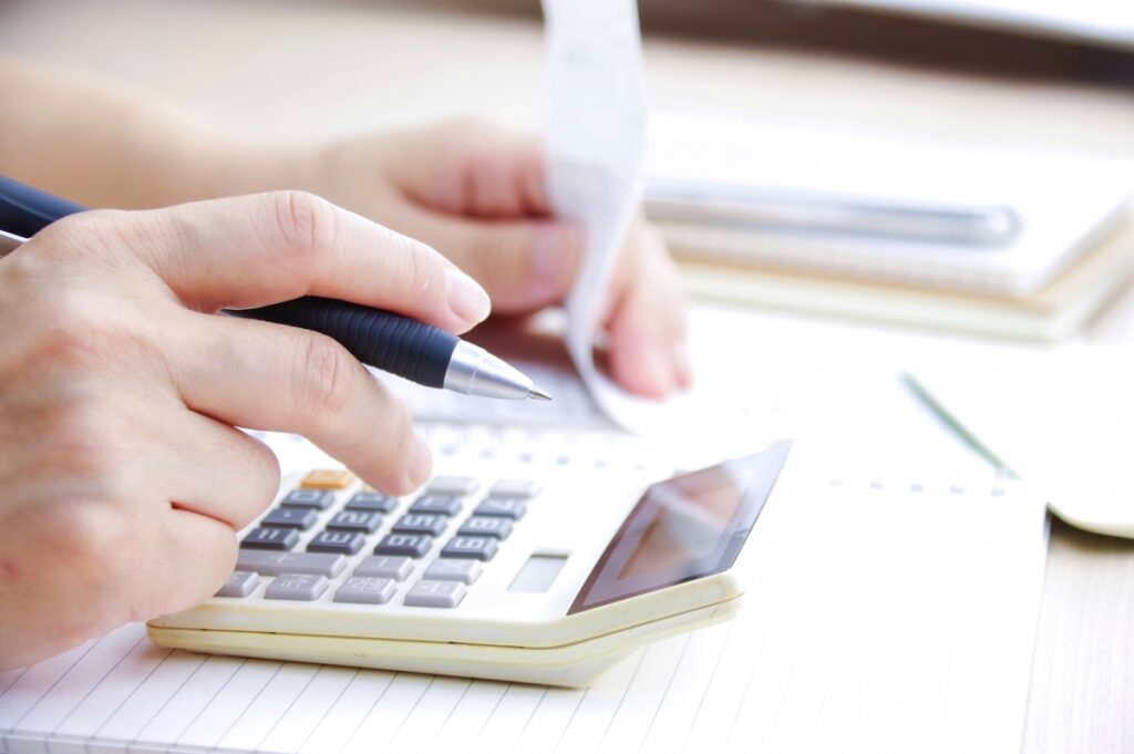電卓と家計簿を使い、ペンを手にしながら住宅ローンの返済額を慎重に計算する手元のアップ。