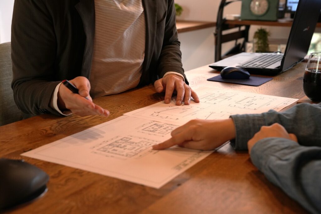 木のテーブルで図面を広げ、土地探し前の家づくりについて打合せをする様子