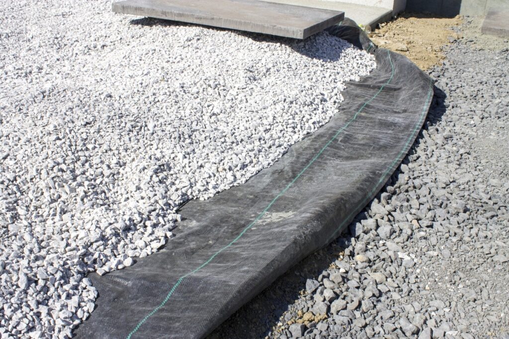 防草シートの上に敷き詰められた白い砂利と外構DIYの施工風景