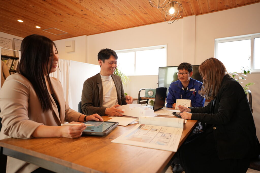 建築現場の打ち合わせスペースで、模型や資料を囲み笑顔で話し合うスタッフ