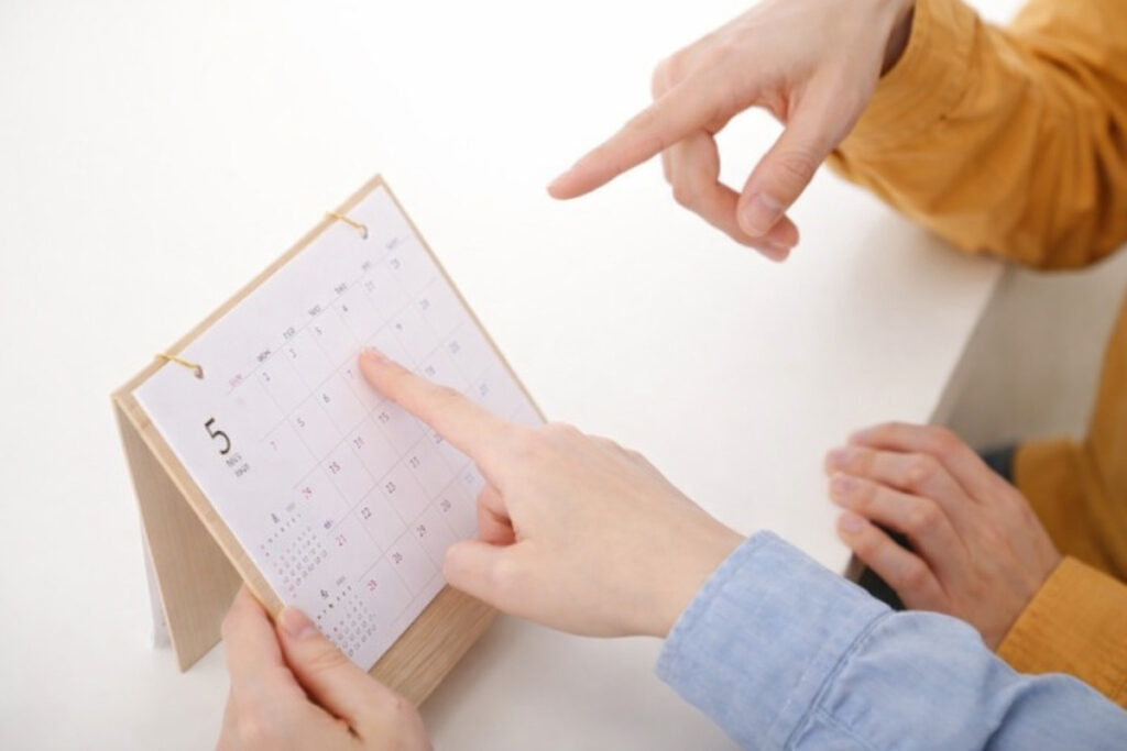 卓上カレンダーを一緒に見ながら、今後の家づくりのスケジュールや次回の打ち合わせ日程を指差しで確認し合うスタッフと施主。