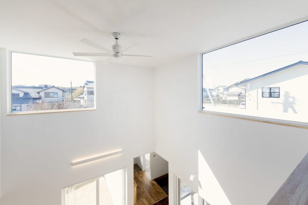 自然光が差し込む大きな窓と、開放的な吹抜けのある白い壁の家づくり事例