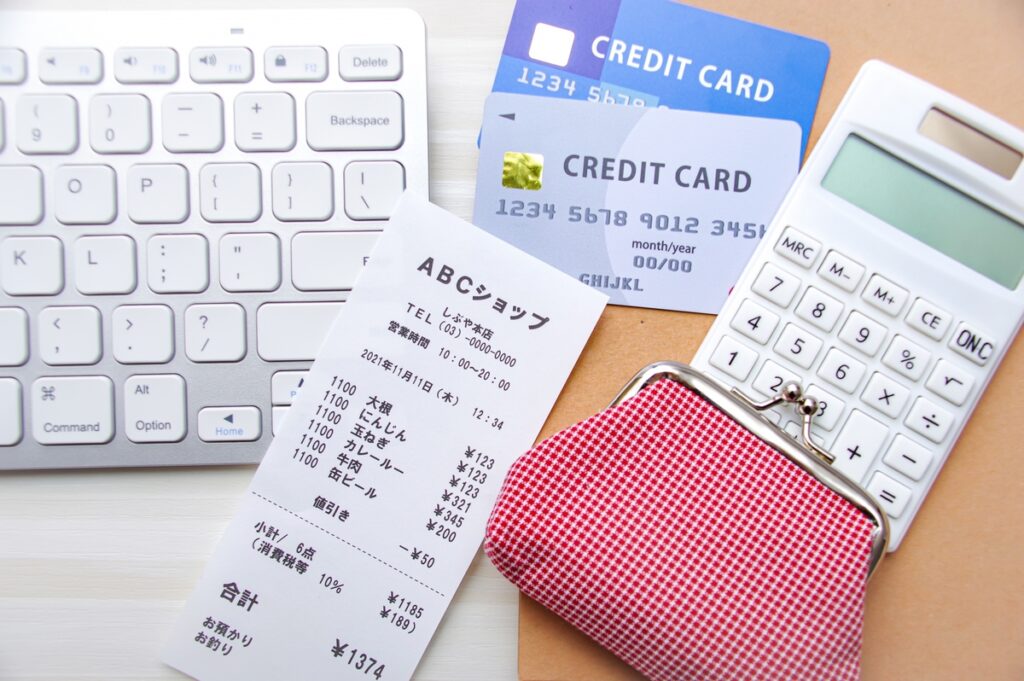 テーブルの上に置かれたスーパーのレシート、財布、クレジットカードと電卓。