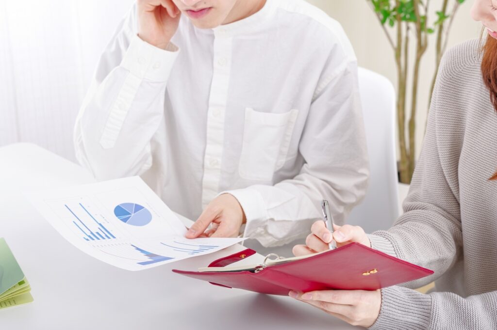 グラフやデータ資料を確認しながら、手帳にメモを取る家づくりの検討風景