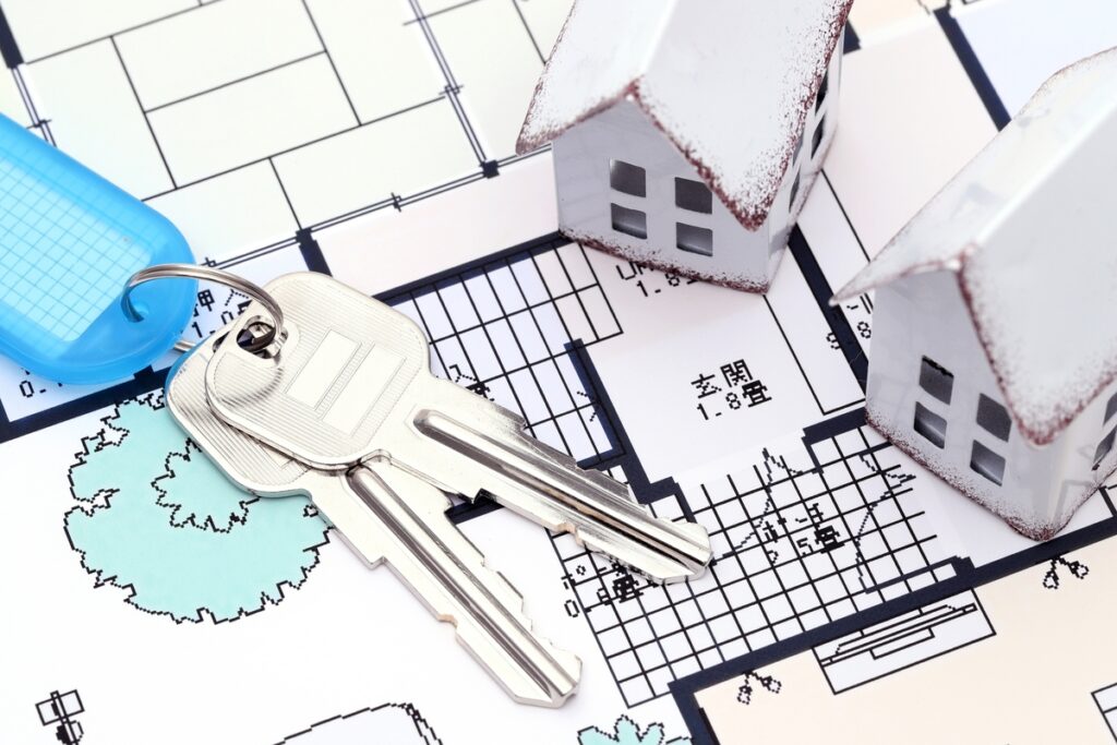 住宅の間取り図の上に置かれた新しい家の鍵と、雪が積もったような加工のミニチュアハウス。